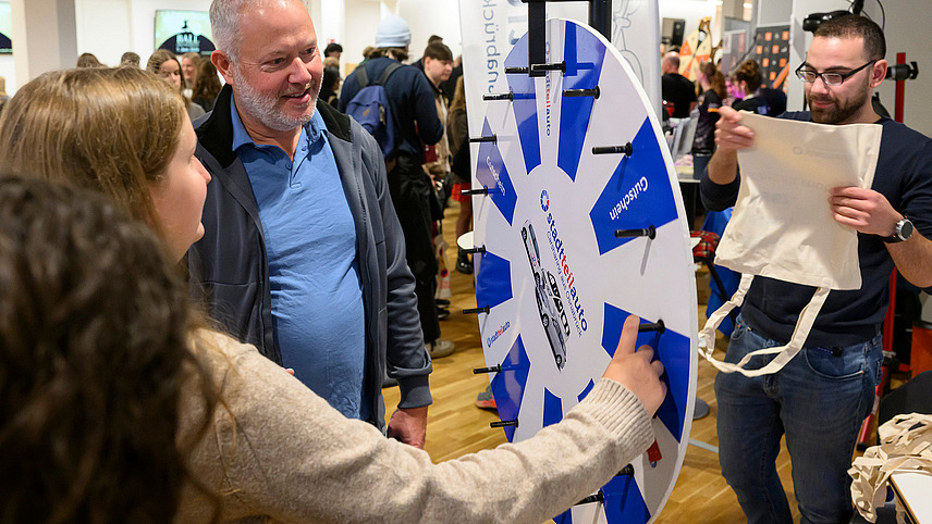 Two people stand at a wheel of fortune