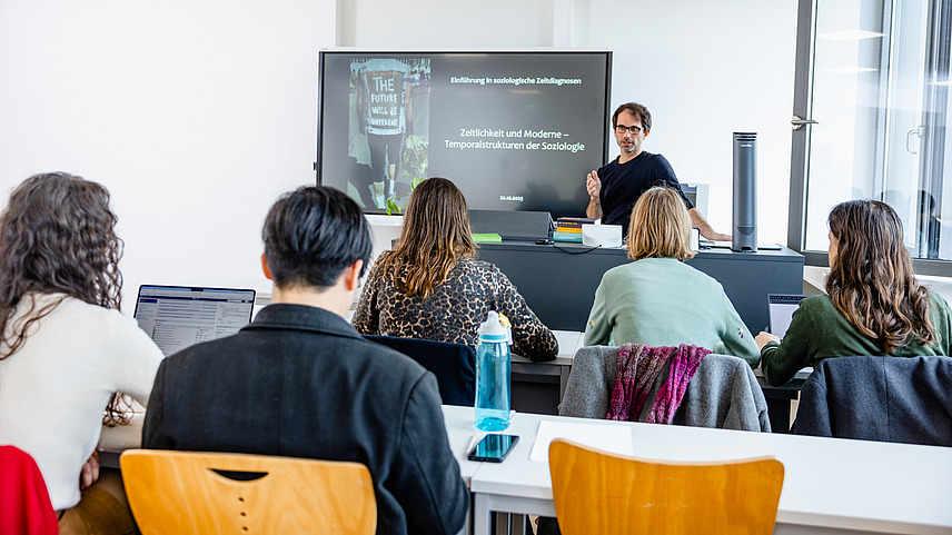 Prof. Gertenbach h&auml;lt einen Seminarvotrag vor Studierenden, im Hintergrund ein Whiteboard mit Pr&auml;sentation, vorne die Studierenden von hinten fotografiert.