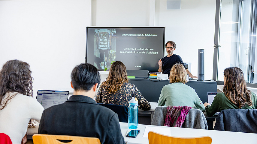 Prof. Gertenbach h&auml;lt einen Seminarvotrag vor Studierenden, im Hintergrund ein Whiteboard mit Pr&auml;sentation, vorne die Studierenden von hinten fotografiert.