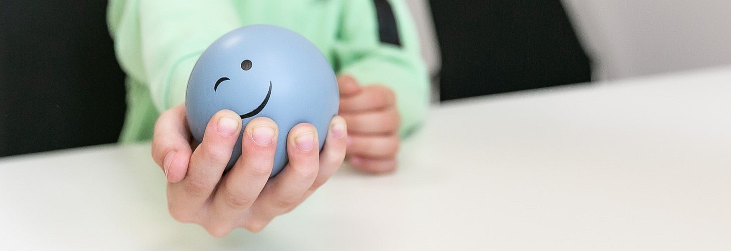 Eine Kinderhand hält einen Ball mit lachendem Gesicht