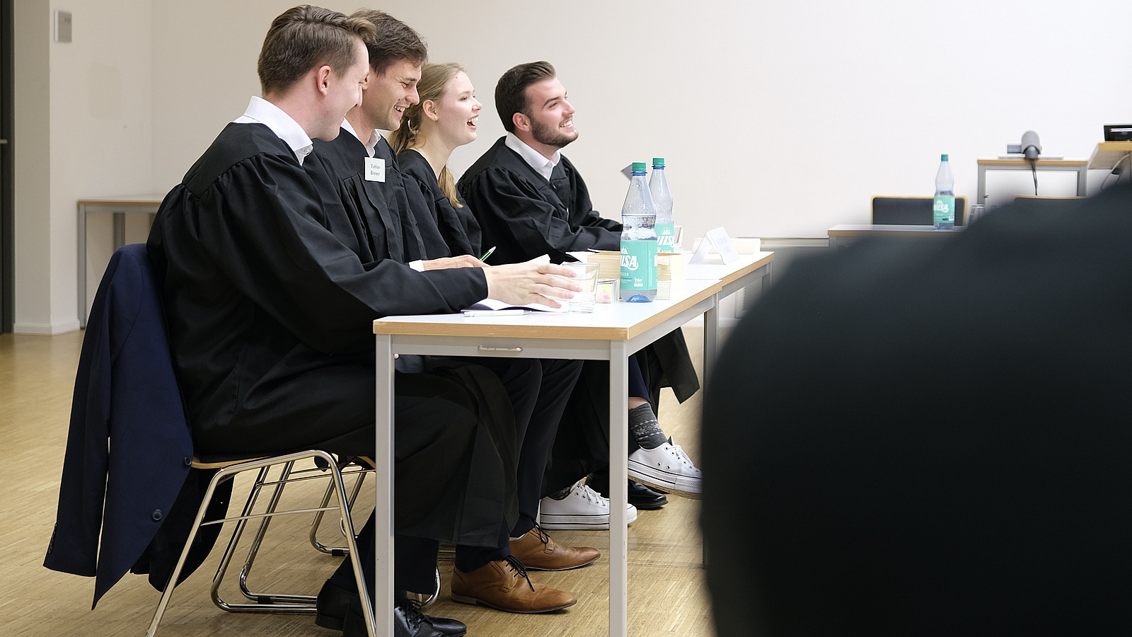 Team aus vier Personen in schwarzen Roben an Tischen sitzend und lachend