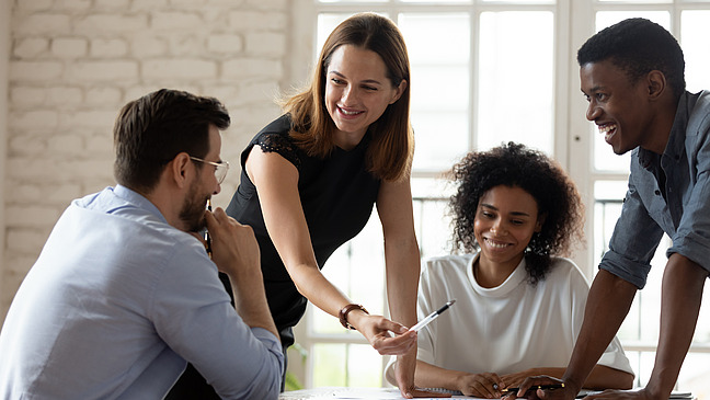 Eine Frau erklärt Personen, die am Tische sitzen die Arbeitsergebnisse.