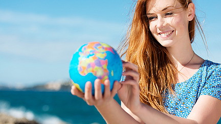 A smiling young woman is holding a globe in her hand.