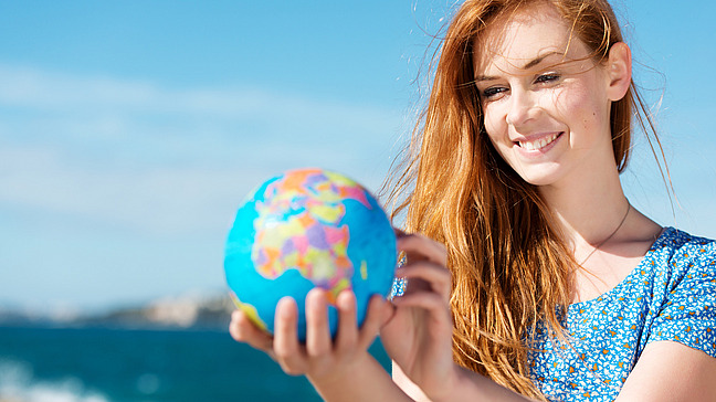 A smiling young woman is holding a globe in her hand.