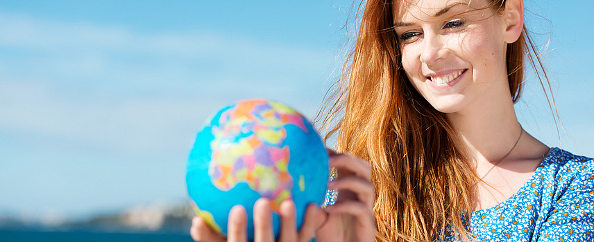 A smiling young woman is holding a globe in her hand.