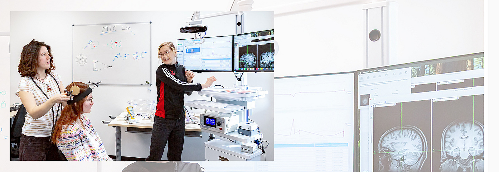 Three women work together in a laboratory. One is sitting on a chair, another is explaining a computer graphic