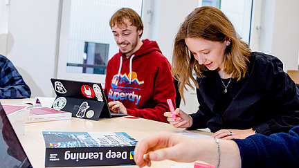 Das Bild zeigt Studierende, die an Laptops arbeiten.