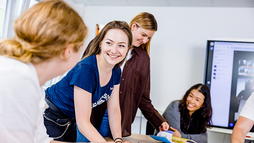 Studierende l&auml;cheln sich an und lehnen &uuml;ber ein Plakat