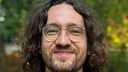 junger Mann mit Locken und Brille lächelt in die Kamera