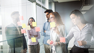 Menschen kleben Post-Its an eine Glasscheibe