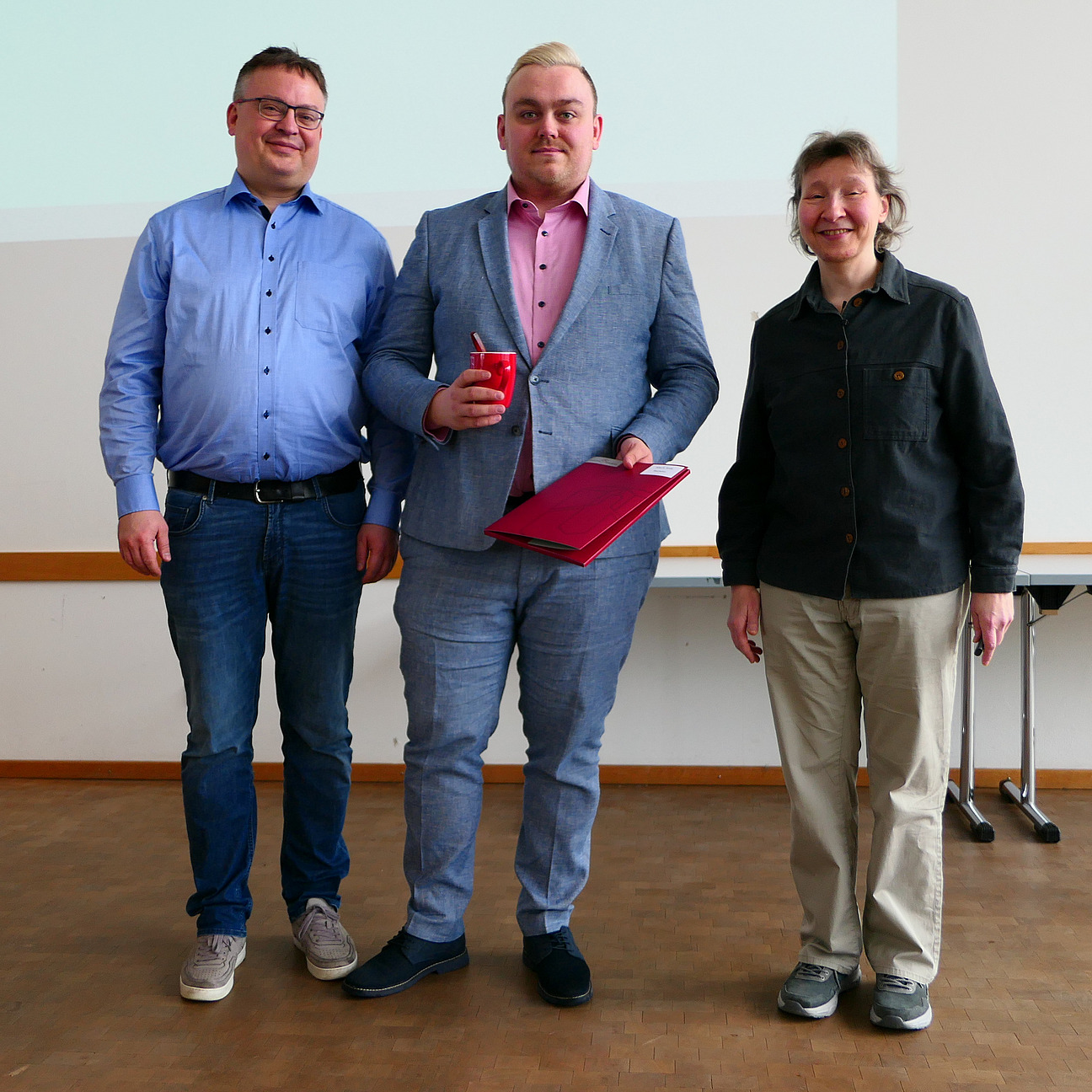 A student stands between the dean and the dean of studies with his degree certificate.