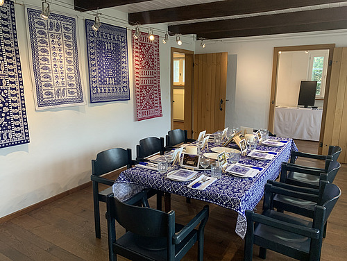 Ein festlich gedeckter Tisch in einem hellen Raum, dekoriert mit traditionellen blau-wei&szlig;en Webteppichen an den W&auml;nden.