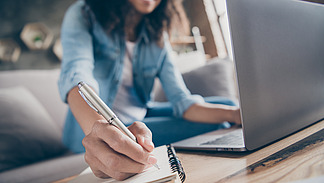 Eine Person arbeitet an einem Notebook und macht sich Notizen auf Papier