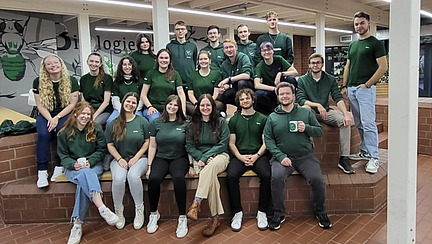 Eine Gruppe von 20 Personen in gr&uuml;nen T-Shirts l&auml;chelt in die Kamera.