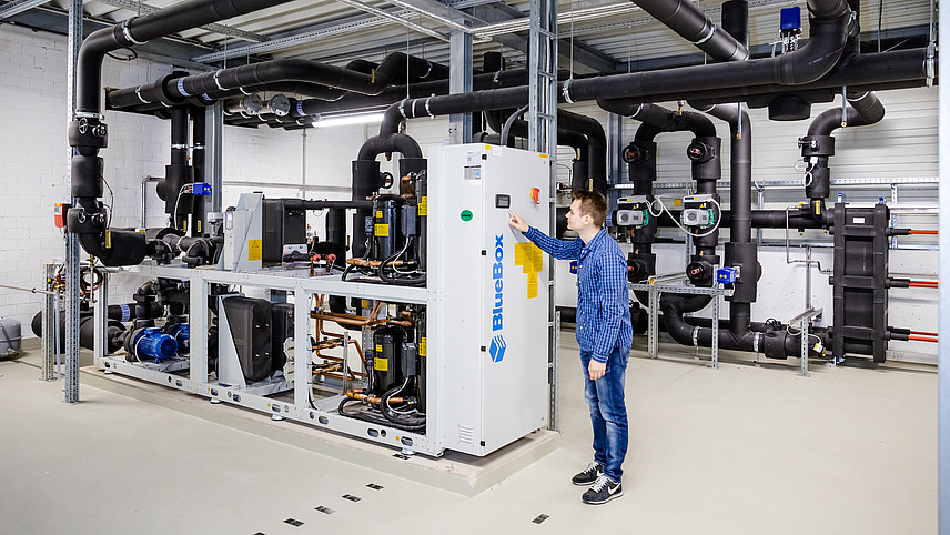 A person is adjusting something on the emergency power generator at the Osnabrück University computer center. Some black pipes and a central, wired box can be seen.