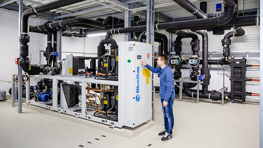 Eine Person stellt etwas am Notstromaggregat des Rechenzentrums der Universität Osnabrück ein. Es sind einige schwarze Rohre und ein zentraler, verkabelter Kasten zu sehen.