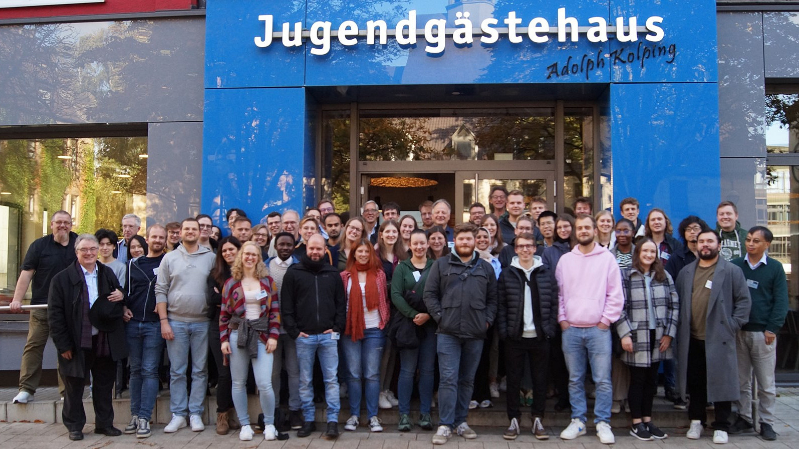 A large group of people is standing in front of a building. The words ‘Jugendgästehaus Adolph Kolping’ can be read above the entrance to the building.