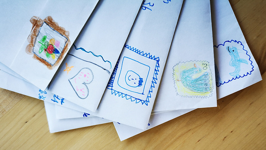 Briefe, die von den Schülerinnen und Schülern beim kommunikativen Schreiben erstellt wurden, liegen gefächert auf einem Tisch. Man sieht selbstgemalte Briefmarekn der Kinder.