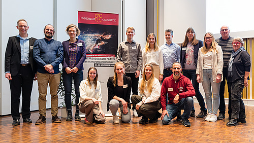 Kollegium des Instituts f&uuml;r Sport- und Bewegungswissenschaften vor einem Banner der DGfE-Tagung.
