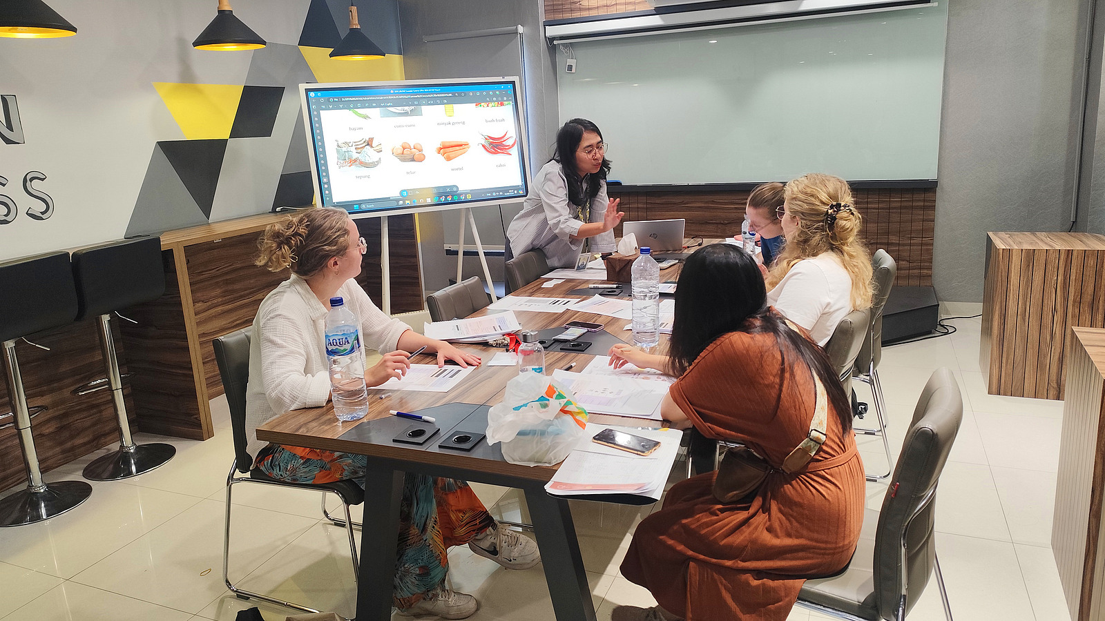 Eine Gruppe von Personen sitzt an einem gro&szlig;en Tisch in einem Raum und diskutiert w&auml;hrend eines Meetings oder Workshops. Auf dem Tisch sind Laptops und Notizen zu sehen, die auf eine gemeinsame Arbeit hindeuten.