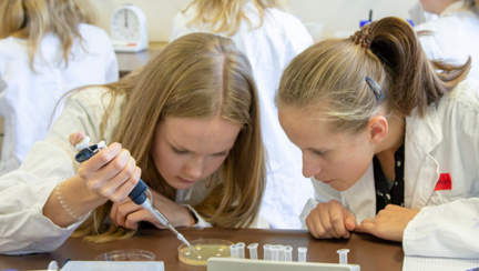 Two pupils are looking at a Petri dish, one is handling a pipette.