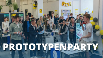 Das Bild zeigt eine Menschenmenge bei einer "Prototypenparty". Eine Person h&auml;lt ein Mikrofon und pr&auml;sentiert etwas, w&auml;hrend die anderen Teilnehmer zusehen.