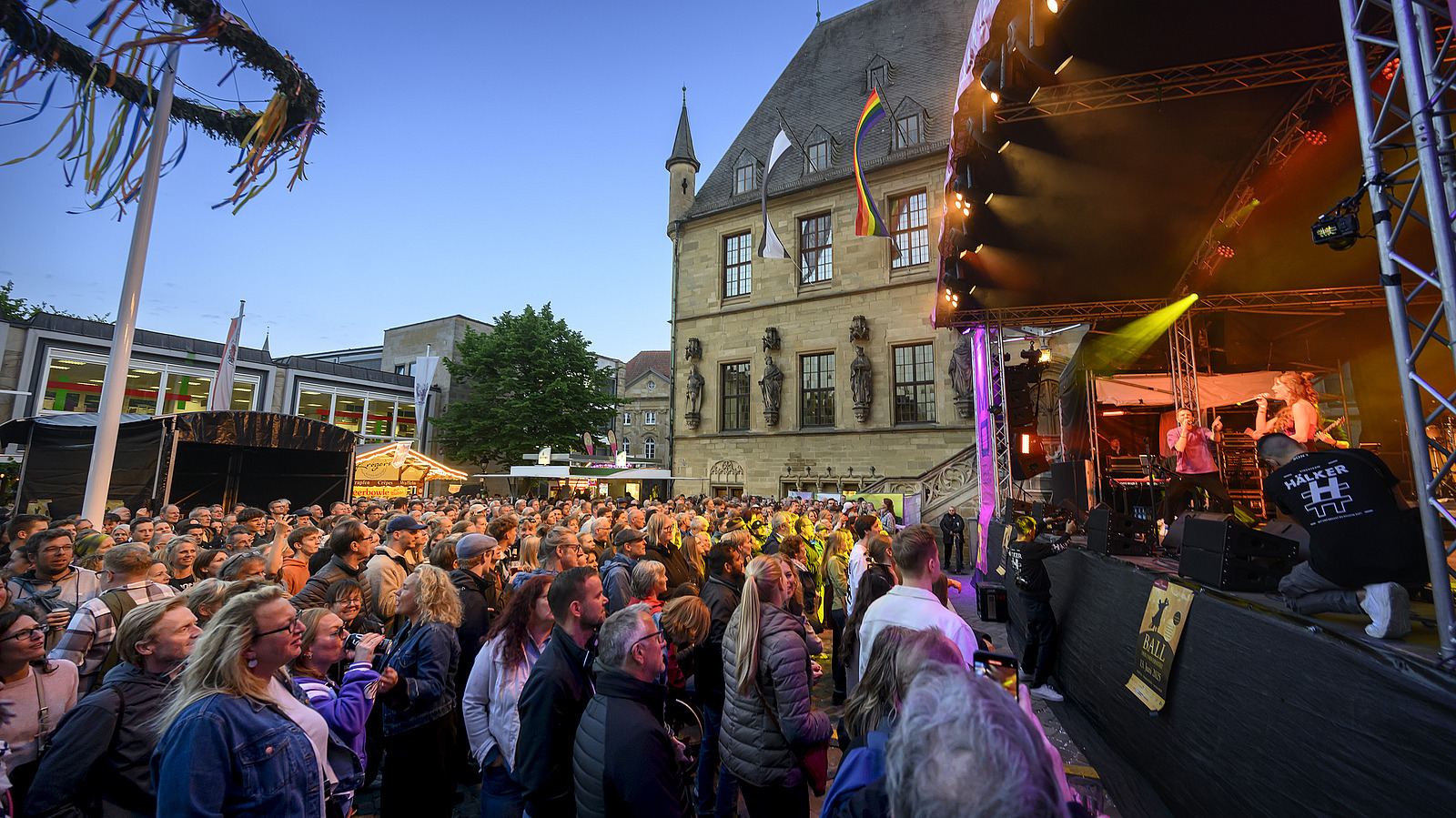 Several musicians on a stage in front of a historic building, audience in front of the stage