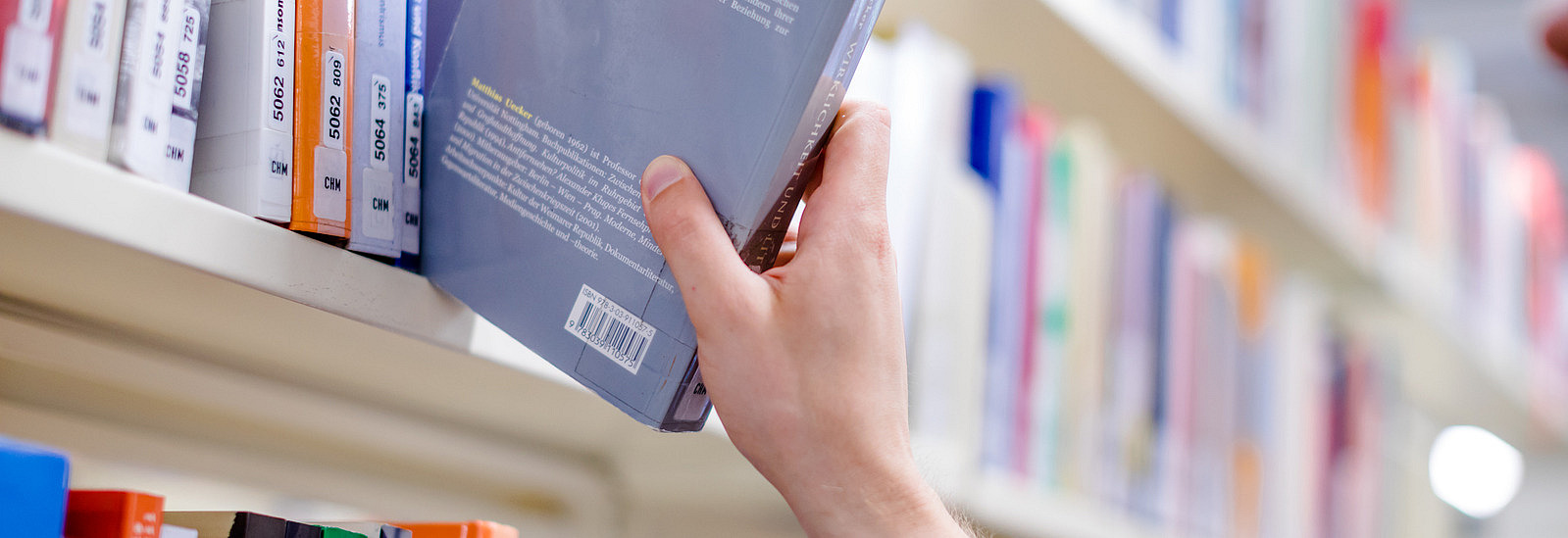 Ein Mann in der Bibliothek Alte Münze zieht ein Buch aus einem Bücherregal.