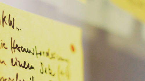 The image depicts a wall covered in sticky notes. 