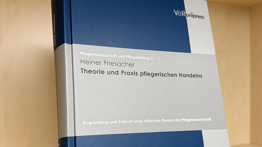 Ein Fachbuch von Heiner Friesacher mit dem Titel "Theorie und Praxis pflegerischen Handelns" steht in einem Regal.