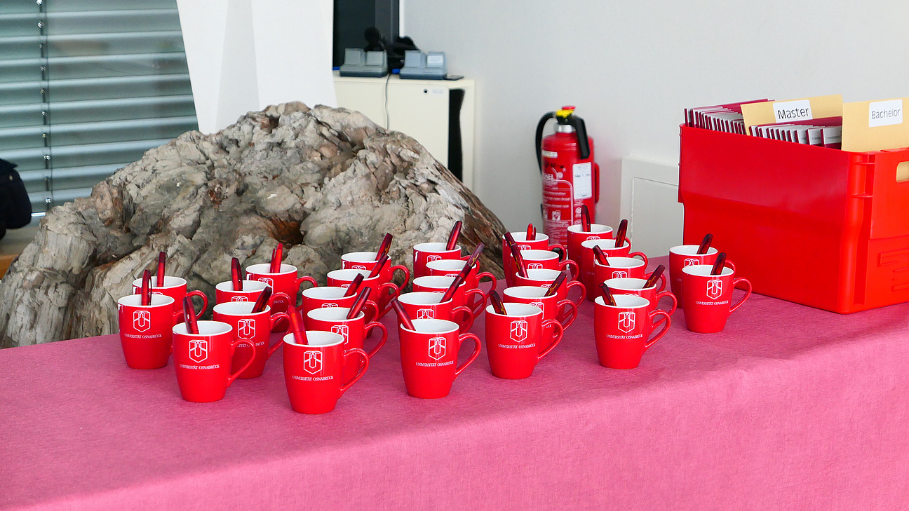 28 Tassen stehen auf einem Tisch. Daneben eine Kiste mit Mappen.