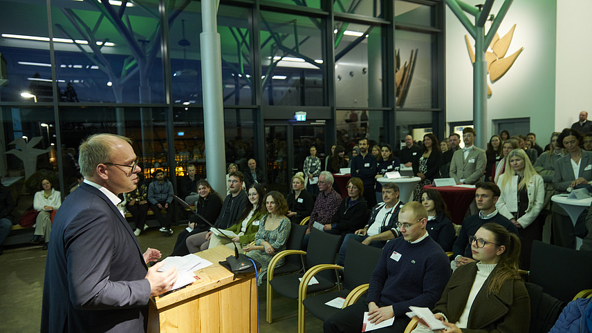 Ein Mann an Rednerpult vor Publikum in einem großen Saal