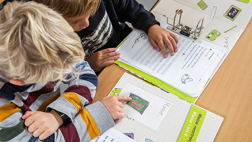 Zwei Schüler sitzen an einem Tisch und arbeiten in ihren wortreich Ordnern.
