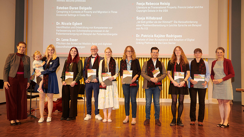 Several people stand on a stage, holding certificates in their hands and smiling into the camera