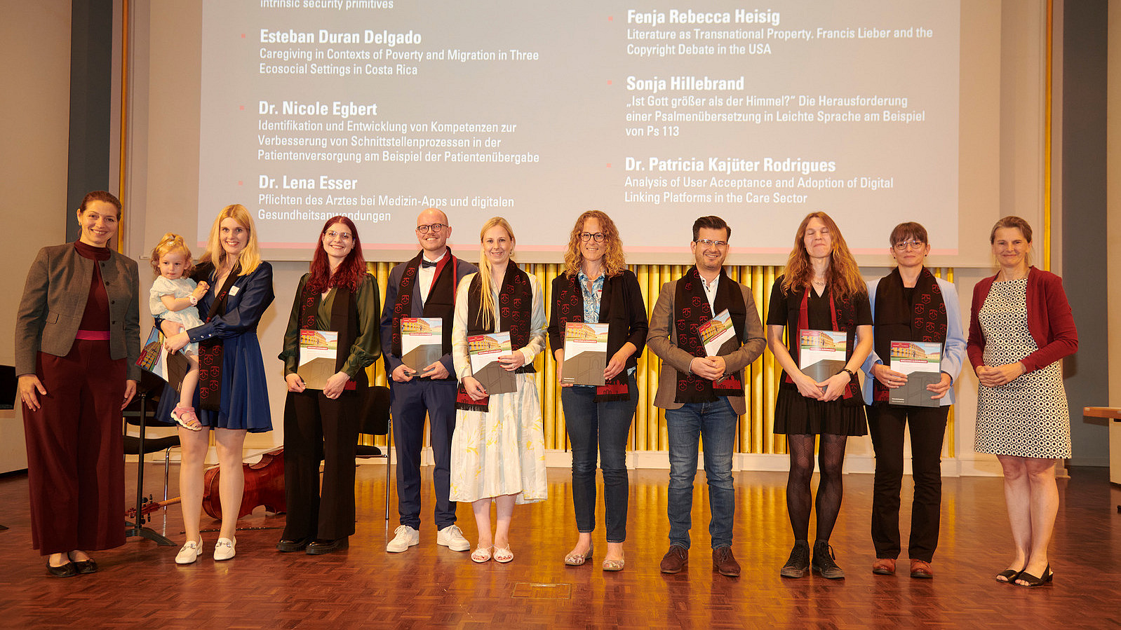 Several people stand on a stage, holding certificates in their hands and smiling into the camera