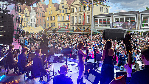 Blick von der B&uuml;hne aus auf die Bigband, davor stehen zahlreiche Zuschauer