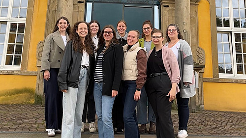 A group of women stand in front of Osnabrück Castle. They smile into the camera.