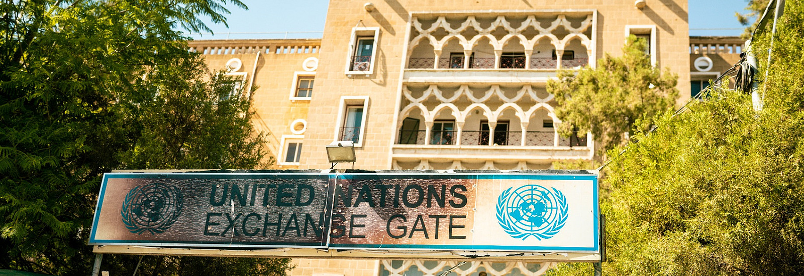 Tor zur alten Pufferzone der UN auf Zypern mit blauem UN-Logo am Tor, dahinter ein verfallenes Geb&auml;ude