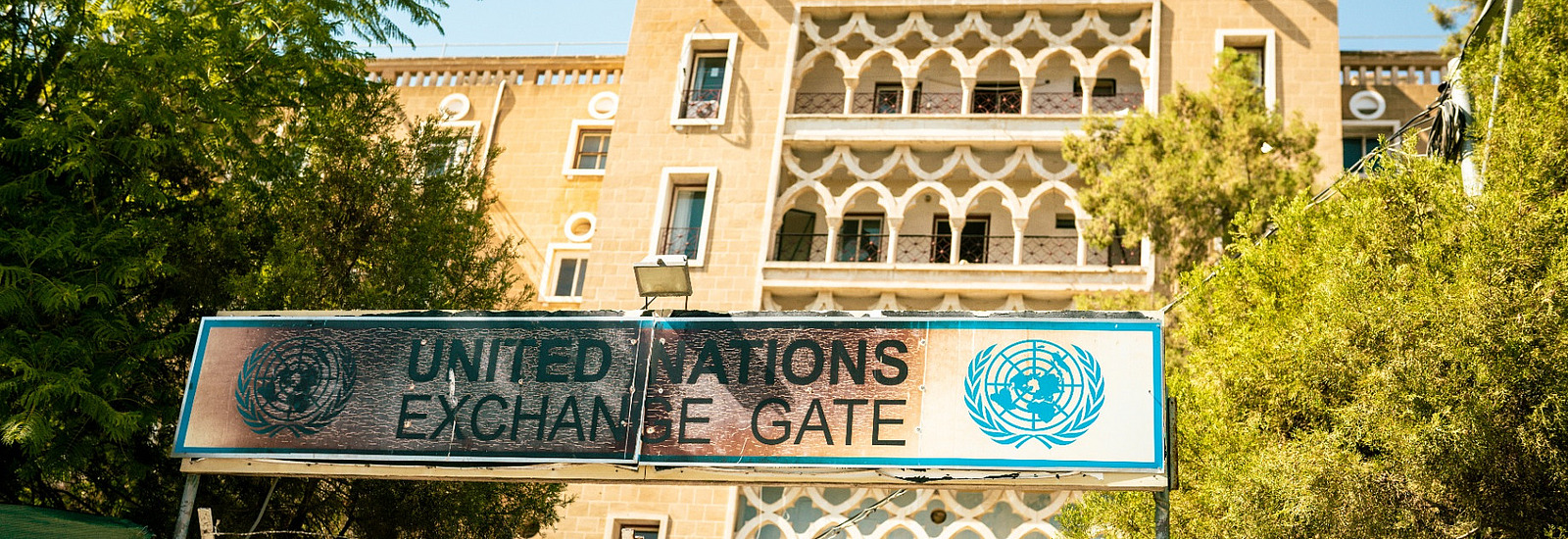 Tor zur alten Pufferzone der UN auf Zypern mit blauem UN-Logo am Tor, dahinter ein verfallenes Gebäude
