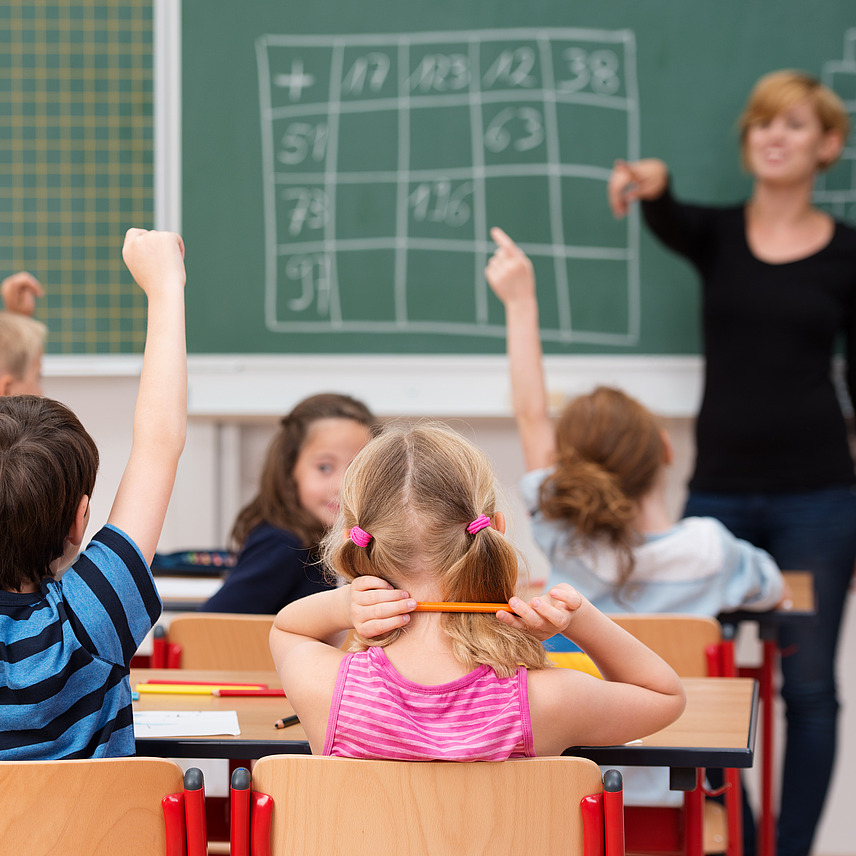 Schulklasse und Lehrerin, die vor einer Tafel steht.