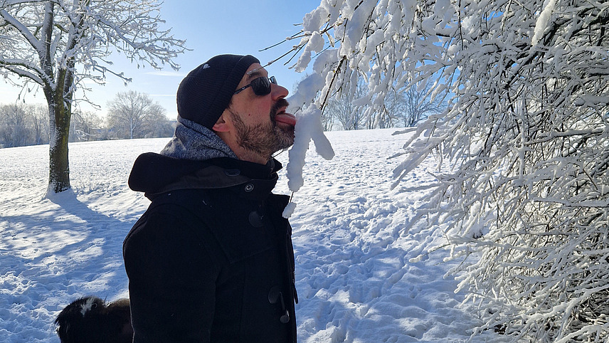 Eine Person steht auf einem verschneiten Weg und schleckt an einem verschneiten Zweig