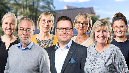 A group of people smile at the camera, with the main biology building visible in the background.