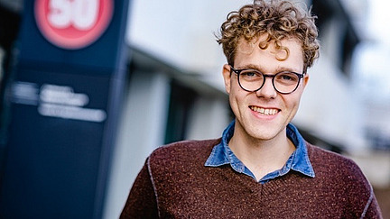 young man with glasses and blonde curly hair smiles into the camera