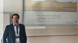 Kai Rohde, im Hintergrund Folie seines Vortrags, auf der das Universitätsgebäude Osnabrück, gelbes Schloss, sowie das Thema seines Vortrags „On the externalities of tech firms" abgebildet sind.  