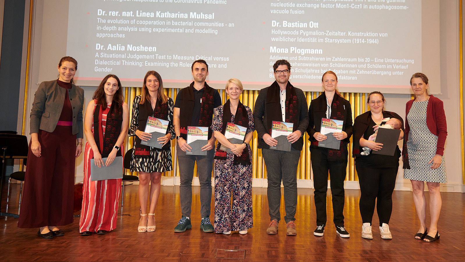 Several people stand on a stage, holding certificates in their hands and smiling into the camera