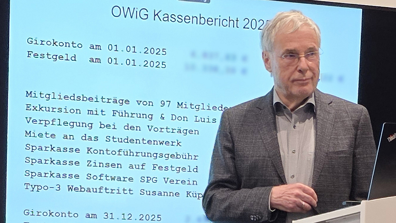 Ein Mann steht an einem Rednerpult vor einer Leinwand mit dem Kassenbericht 2025