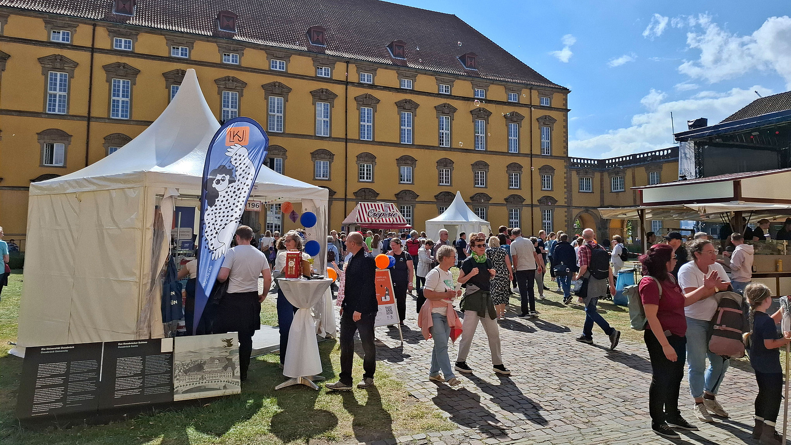 Information stands, food stalls and visitors in front of a castle.