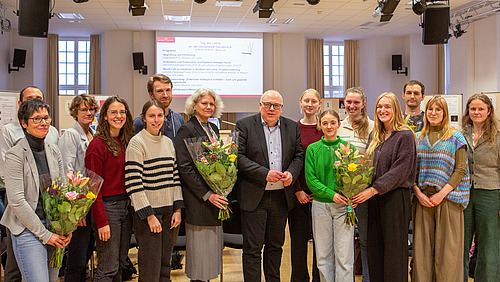 Männer und Frauen stehen nebeneinander, lächeln und halten einen Blumenstrauß in den Händen.
