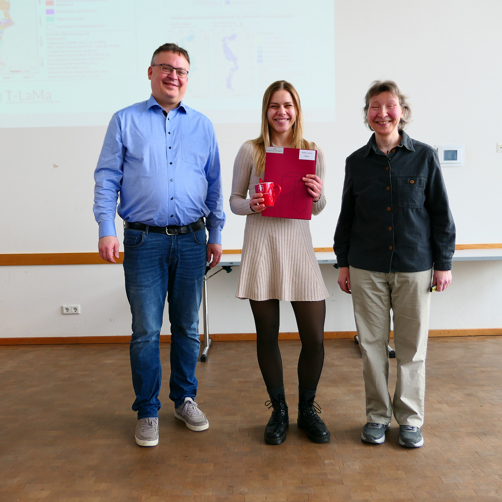 Eine Studentin steht mit ihrem Abschlusszeugnis zwischen Dekan und Studiendekanin.