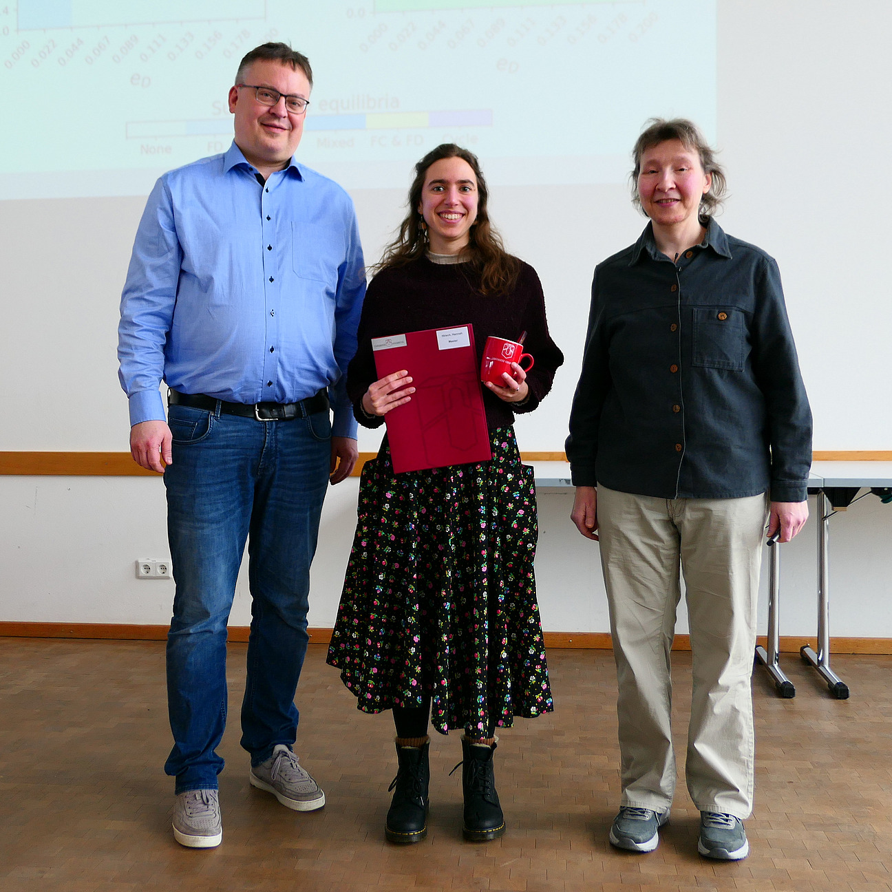 Eine Studentin steht mit ihrem Abschlusszeugnis zwischen Dekan und Studiendekanin.